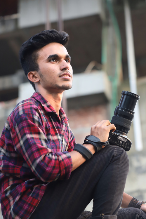 Free A young man in casual attire holding a DSLR camera, sitting outdoors. Stock Photo