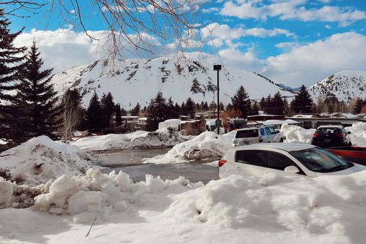 A serene winter view of cars parked by snow-covered mountains in Jackson, WY.