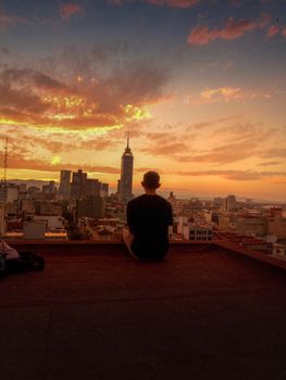 A person sitting on a rooftop overlooking the Mexico City skyline with a vibrant sunset.