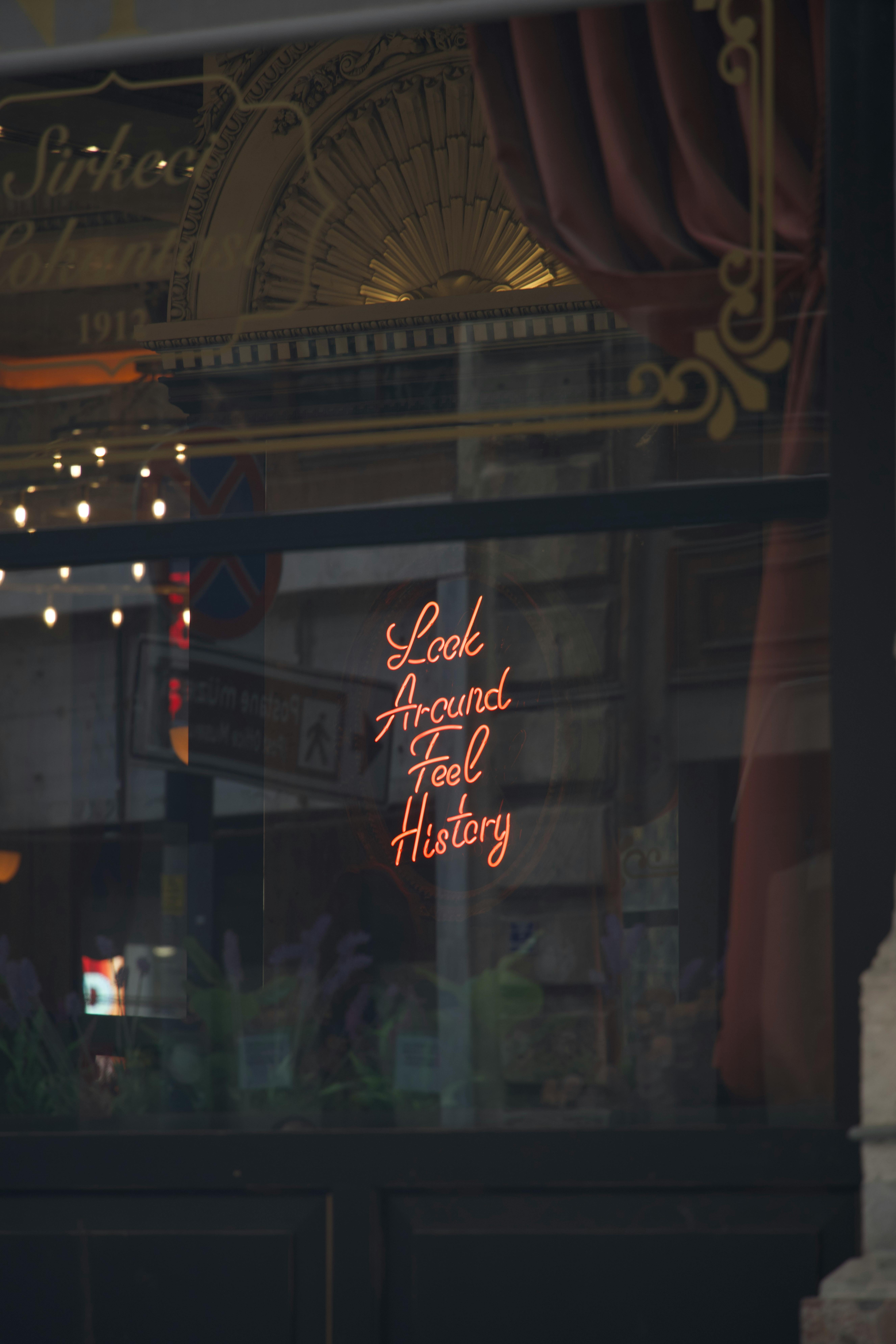 Charming vintage window with neon sign 'Look Around Feel History' reflecting historical ambiance.