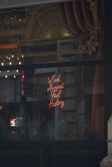 Charming vintage window with neon sign 'Look Around Feel History' reflecting historical ambiance.