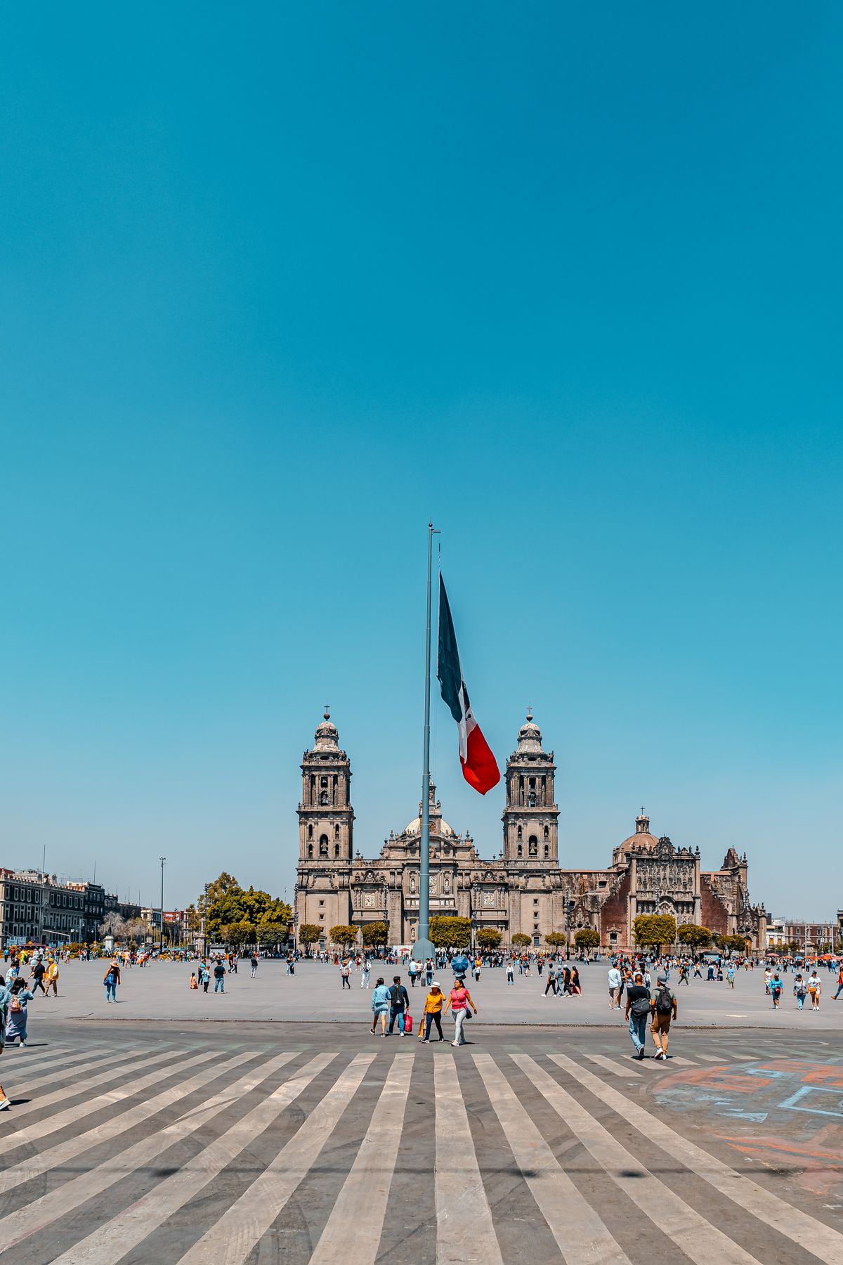The Metropolitan Cathedral and Mexican flag against a clear blue sky in Mexico City's Zócalo.