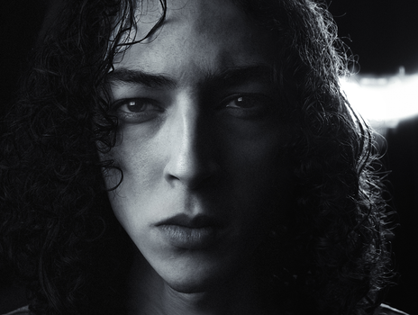 Close-up black and white portrait of a young man with curly hair in London studio lighting.