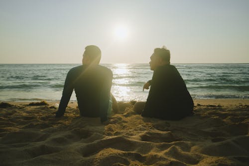 Two men sitting on the beach at sunset