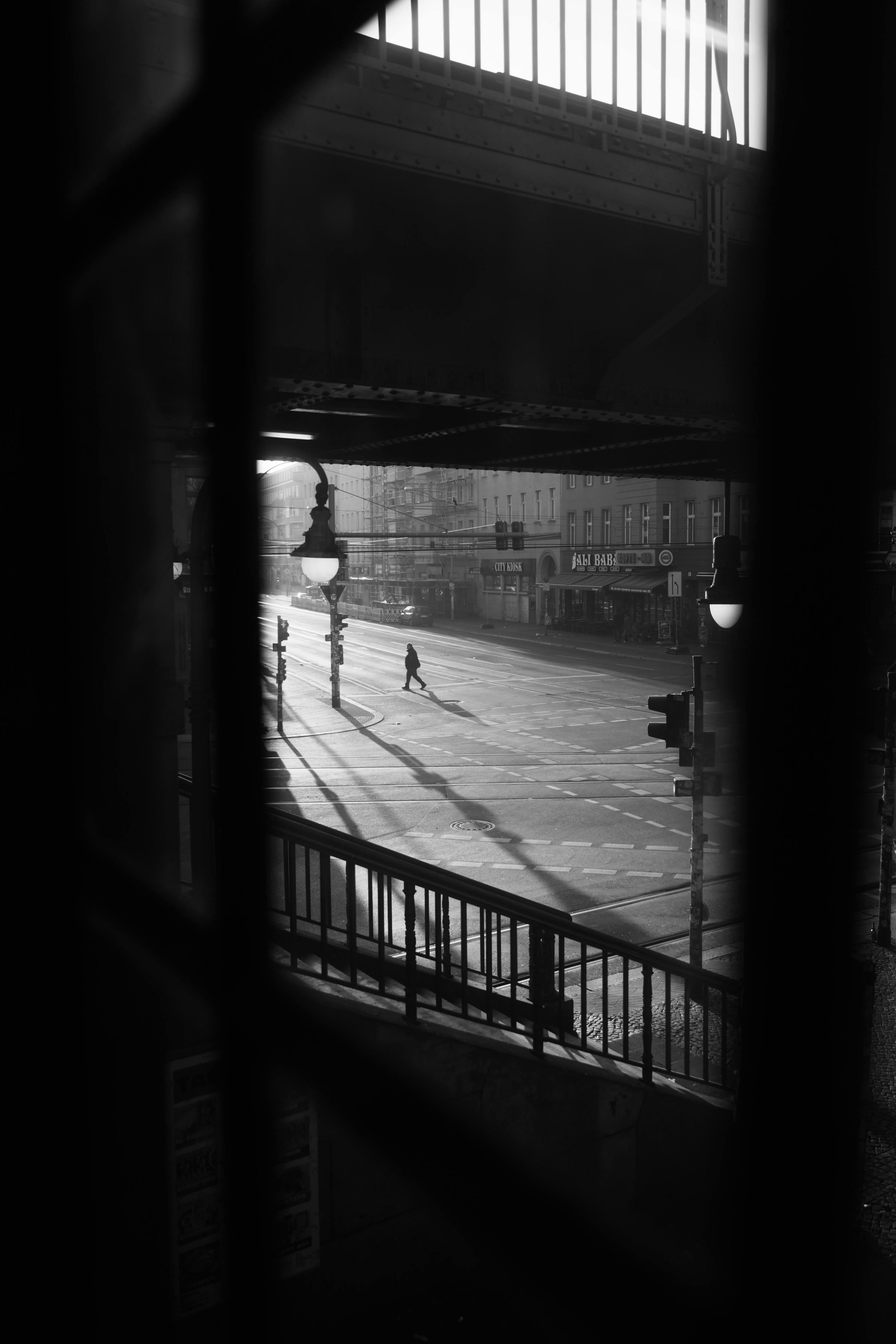 Black and white view of a pedestrian in Berlin crossing under a bridge, showcasing urban architecture.