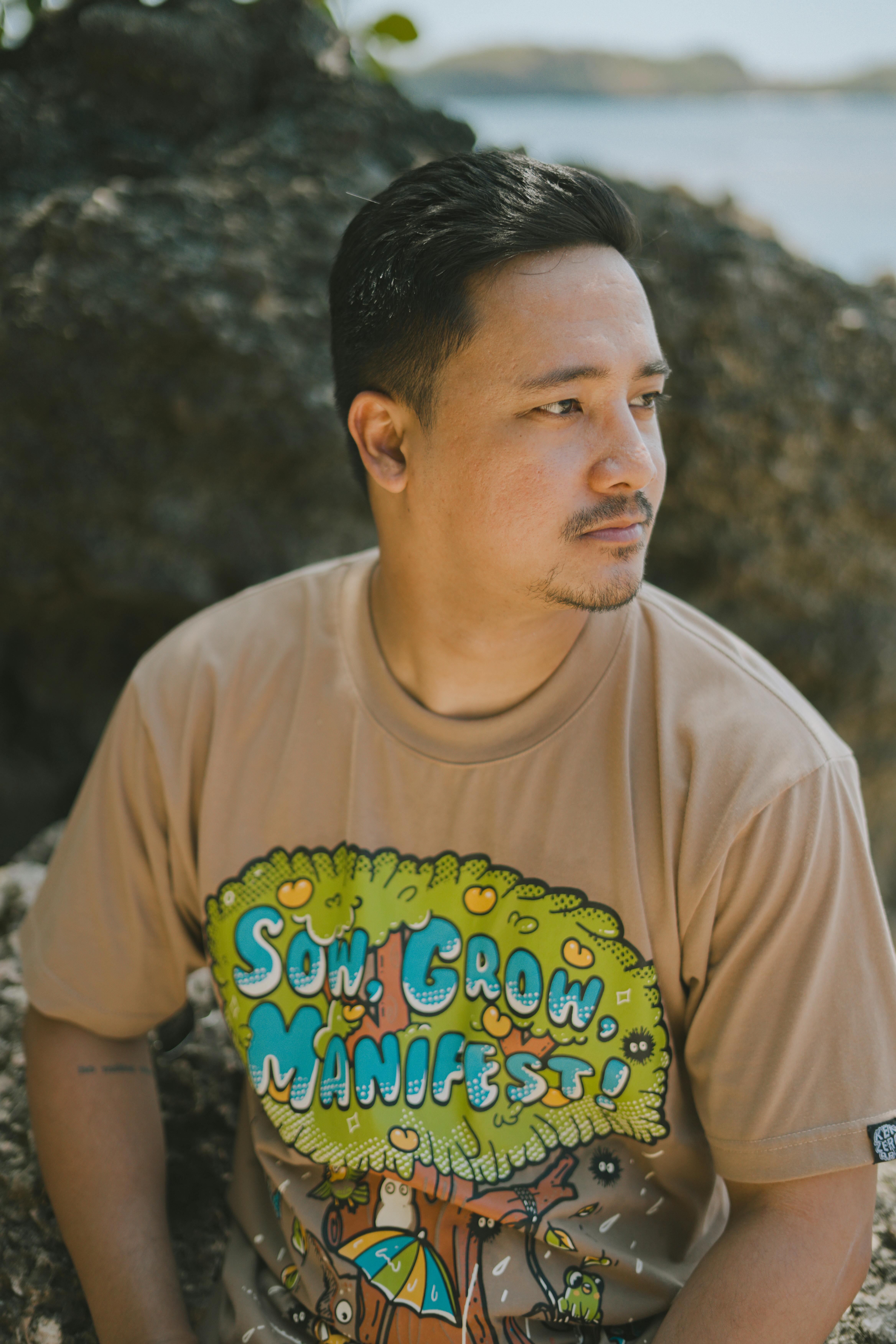 A thoughtful man in a graphic t-shirt sits by the seaside rocks in Bolinao.