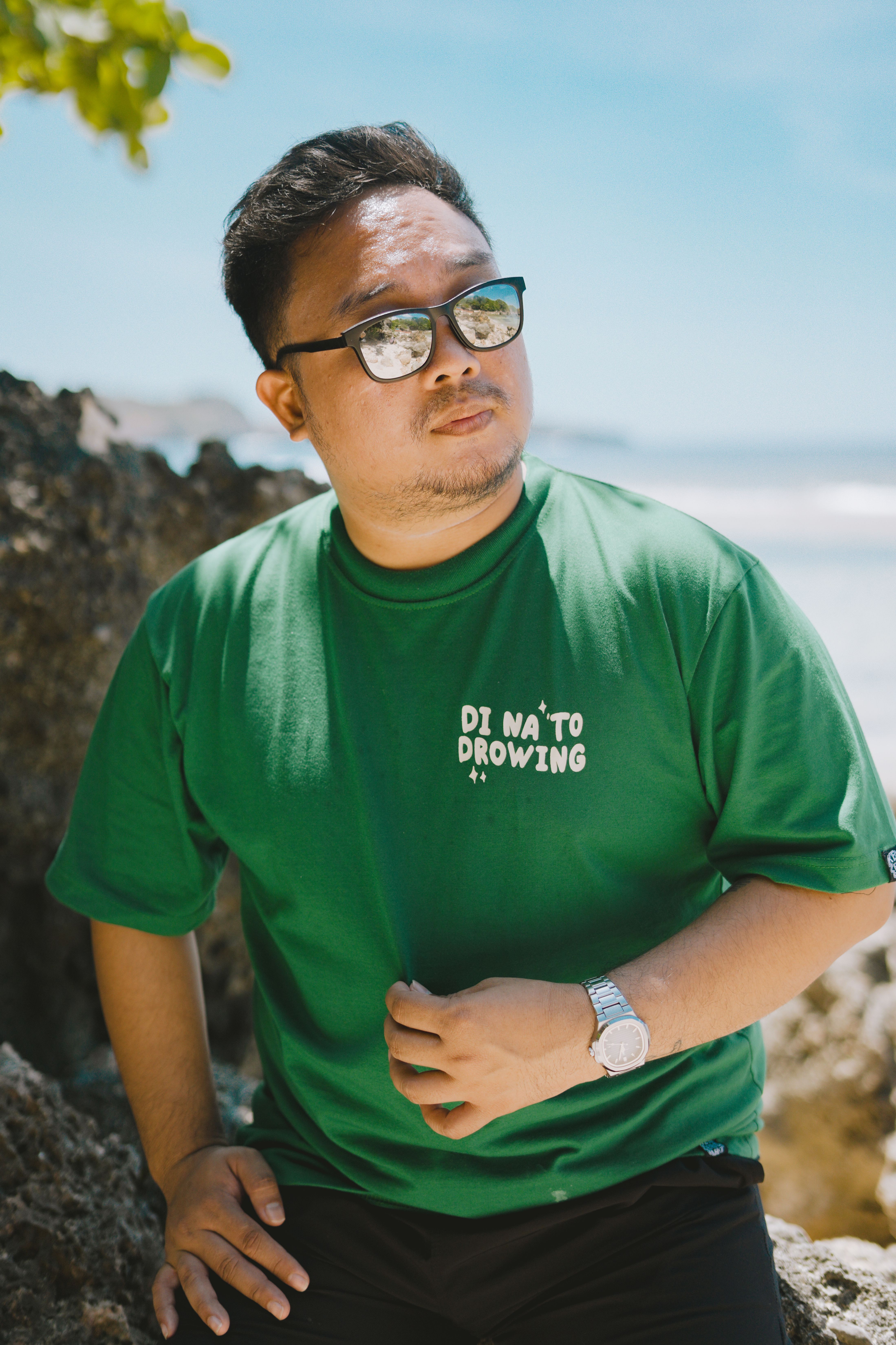 Stylish man in sunglasses and green shirt enjoying a sunny day at Bolinao beach.