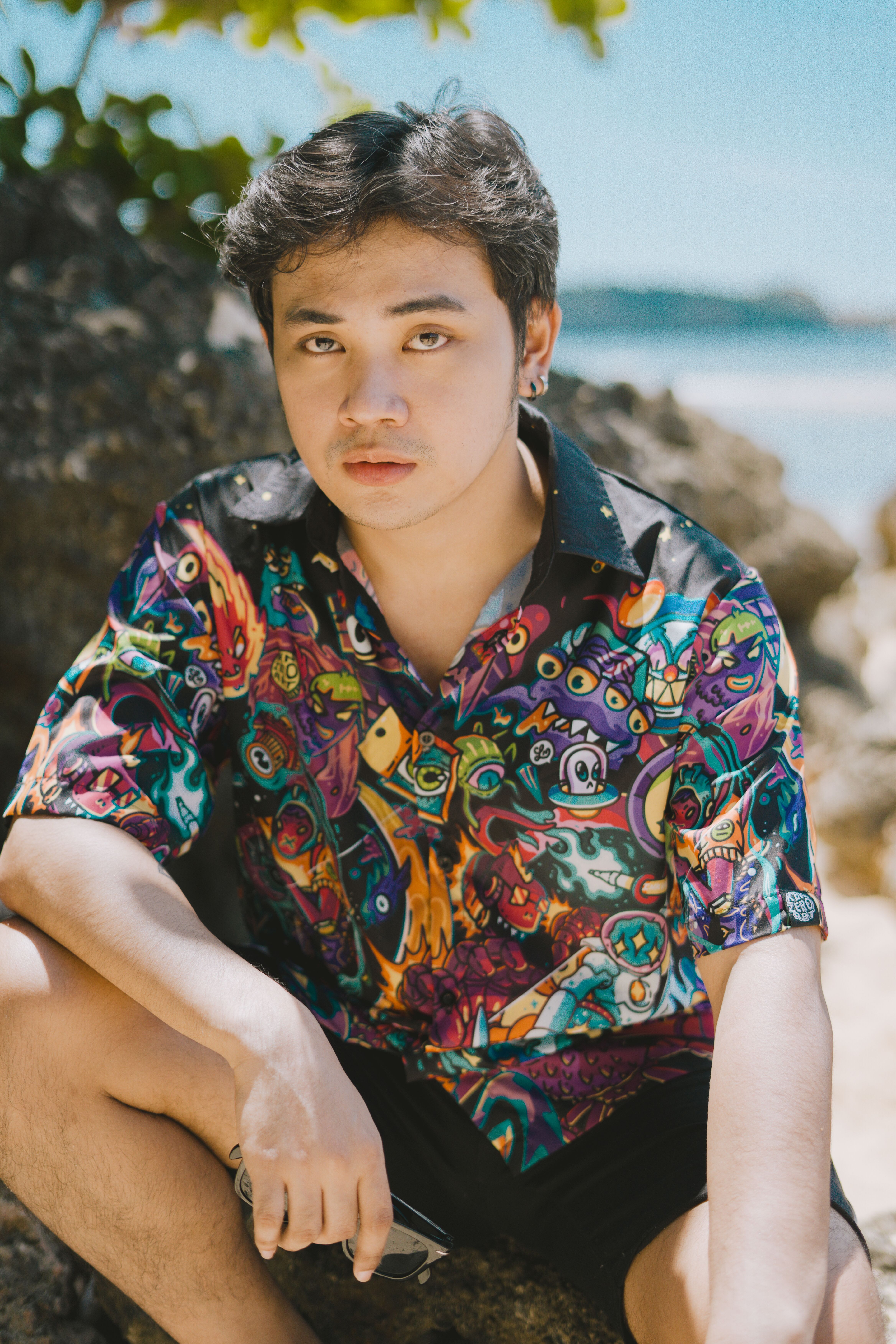Portrait of a young man in a colorful shirt relaxing by rocks on a sunny tropical beach.