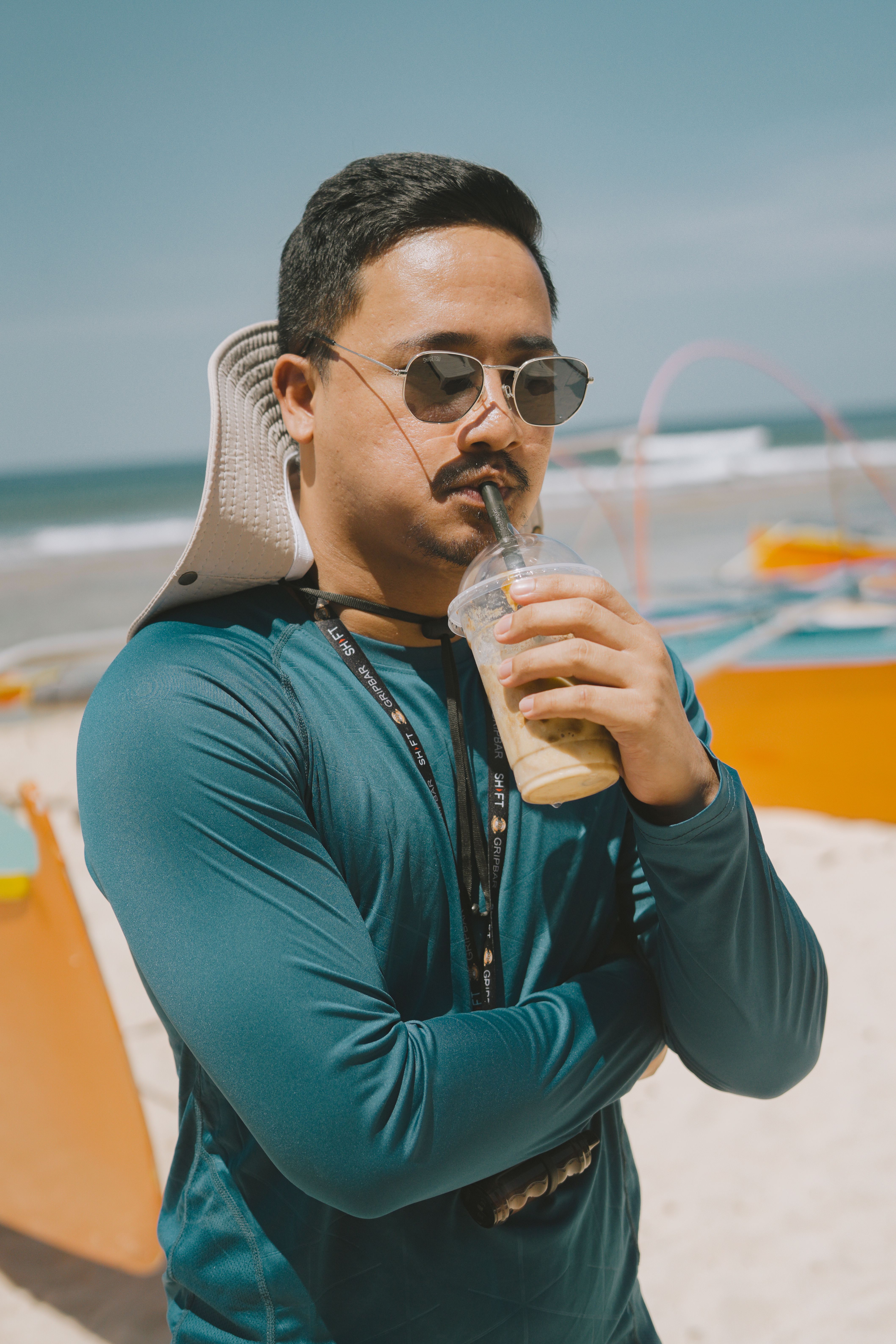 Relaxed man sipping a drink on a sunny Bolinao beach day, wearing sunglasses and casual attire.