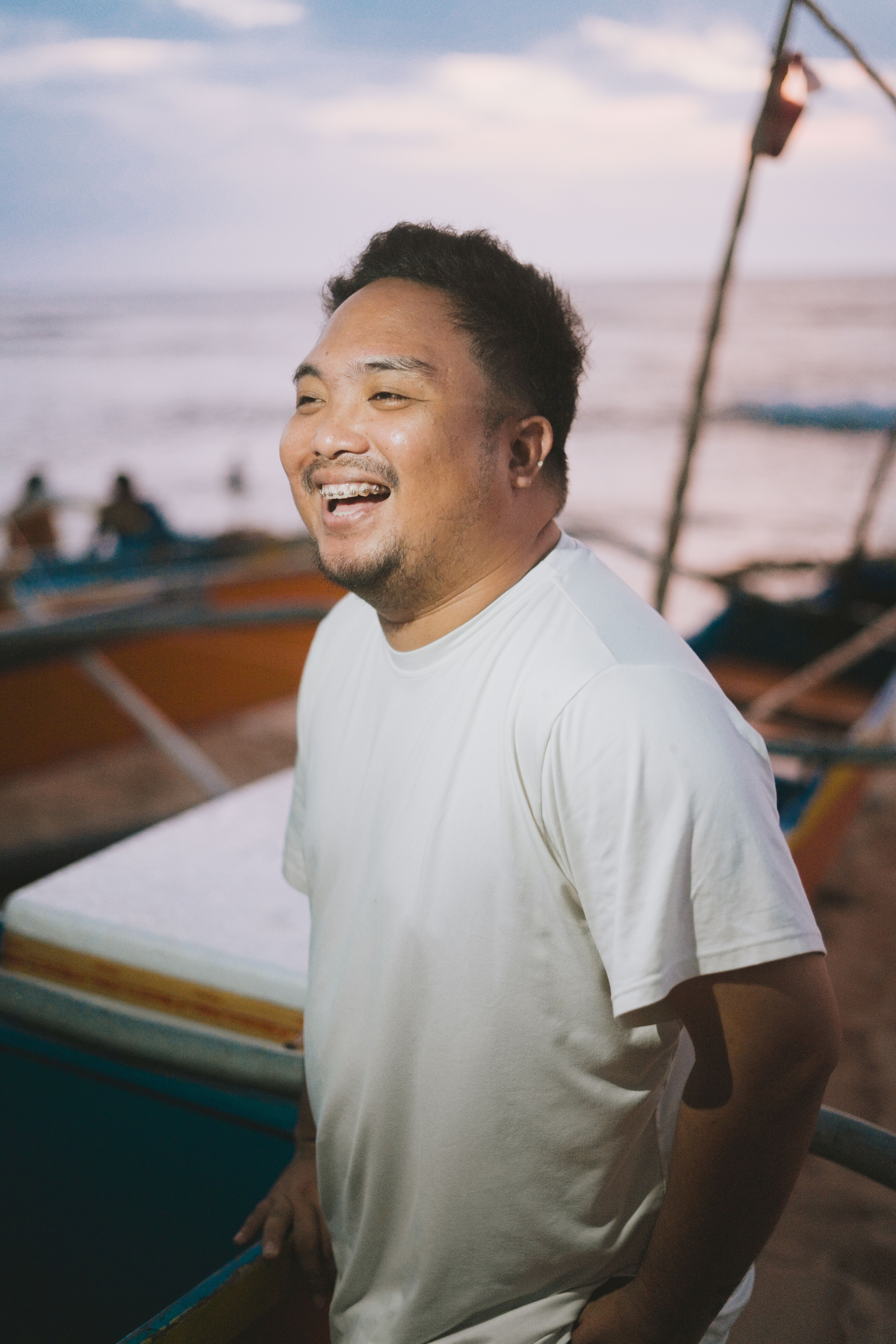 Fotografía de referencia de un hombre riéndose junto al mar, con camiseta blanca y el logotipo TimeParche superpuesto como mockup