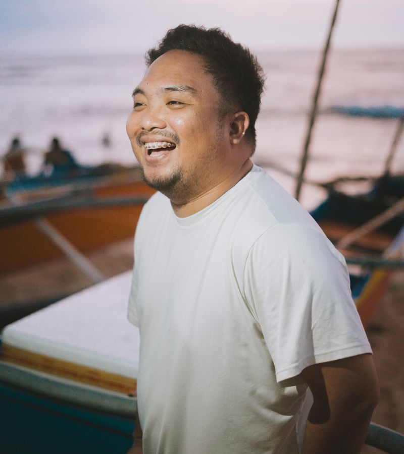 Fotografía de referencia de un hombre riéndose junto al mar, con camiseta blanca y el logotipo TimeParche superpuesto como mockup