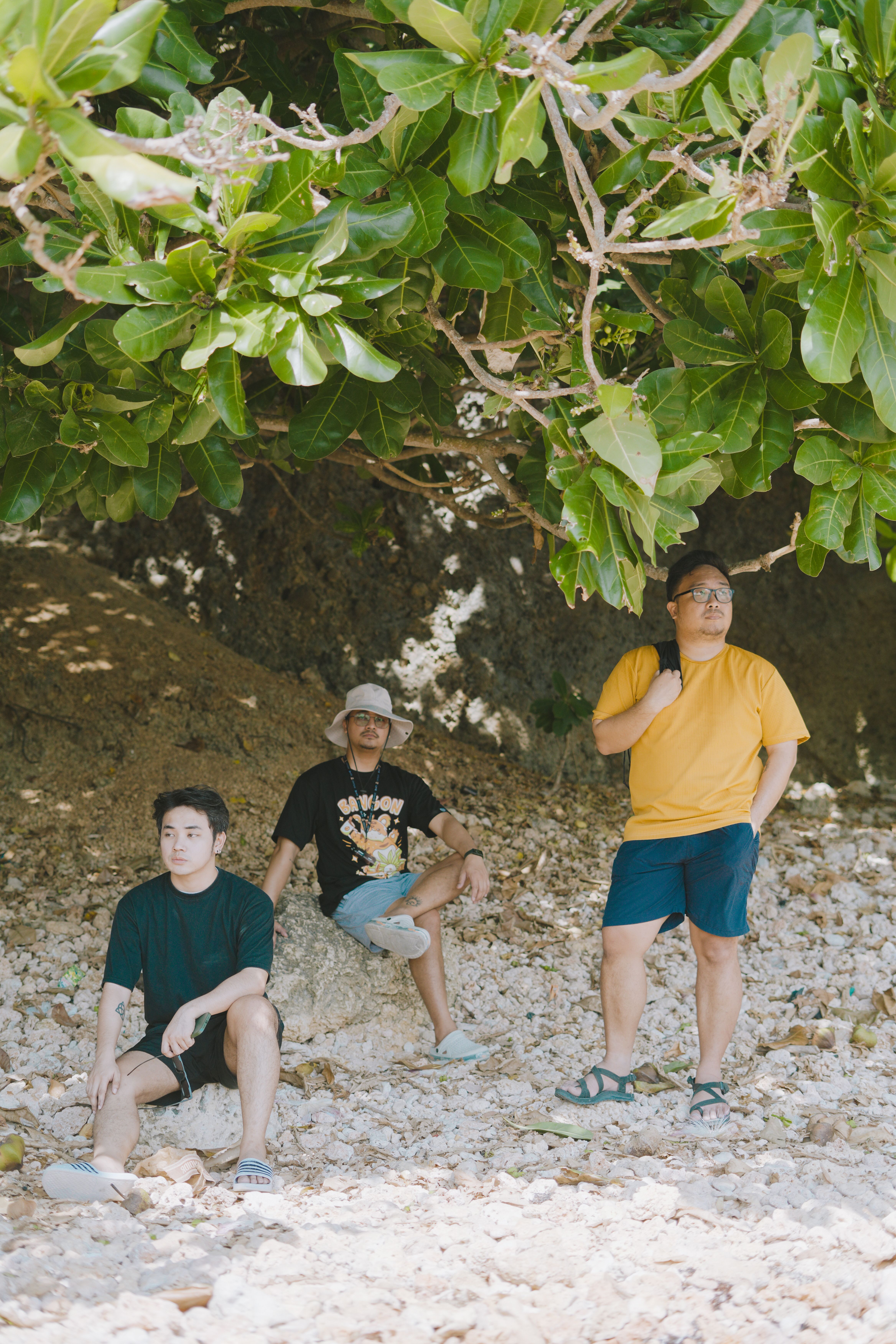 Three men in casual summer attire sitting under tropical foliage in Bolinao, Philippines.