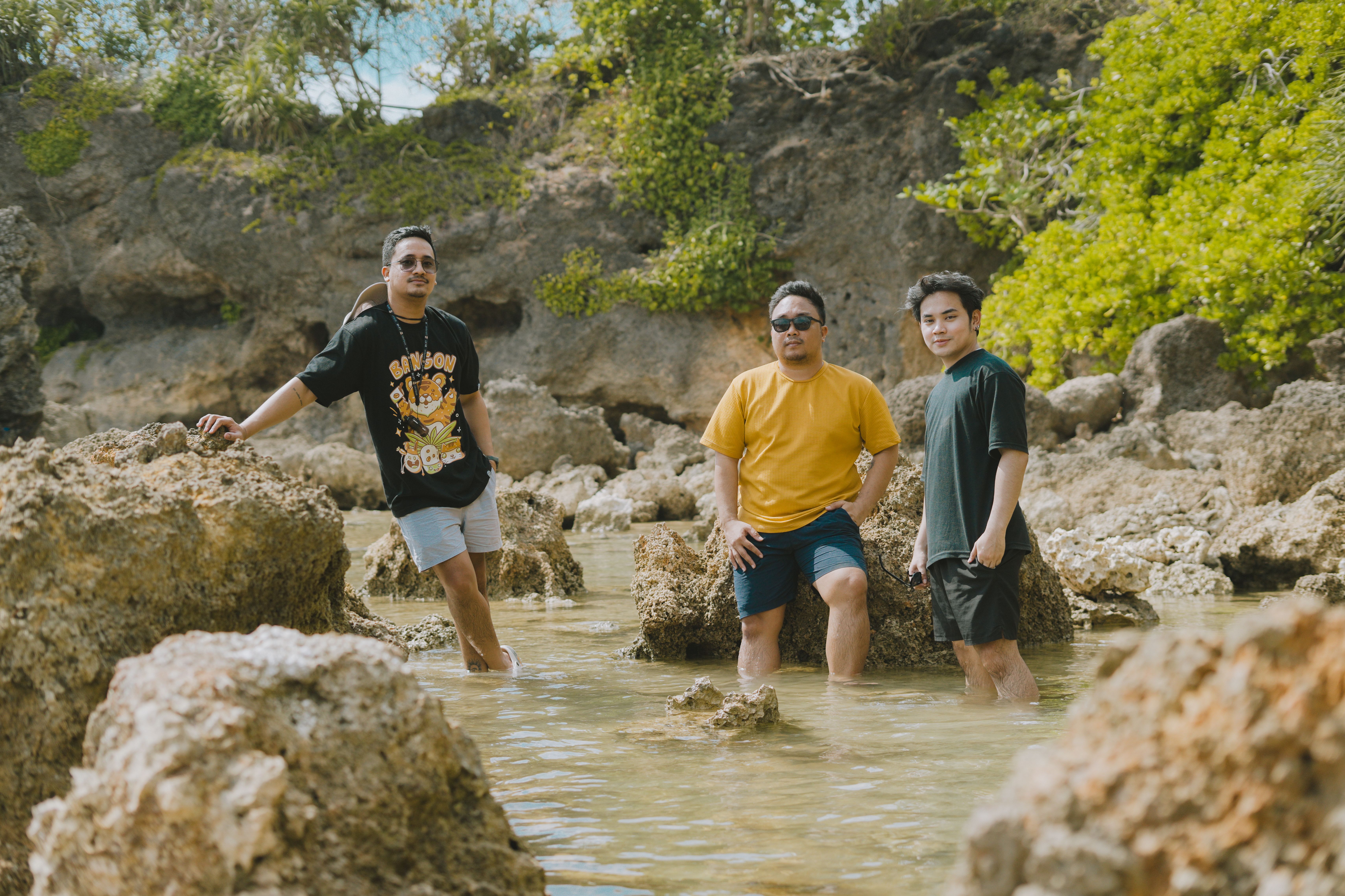 Three men enjoying the rocky shoreline of Bolinao, Pangasinan, Philippines, in a casual setting.