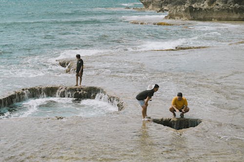 Three people are standing in the ocean near a hole