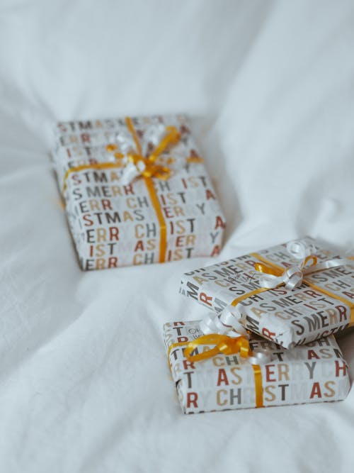 Three wrapped presents on a bed with yellow ribbon