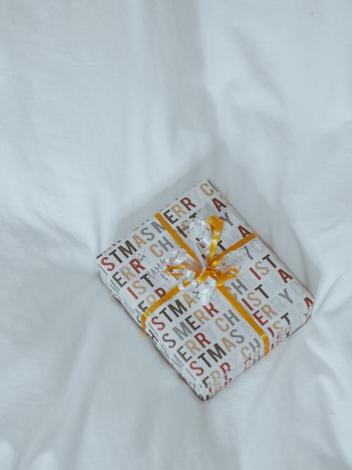 A wrapped gift on a white bed with a ribbon
