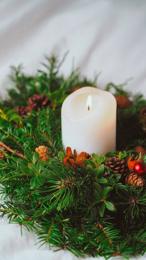 A candle is placed in a wreath with pine cones and evergreen
