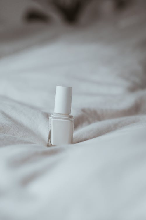 A bottle of nail polish sitting on top of a bed