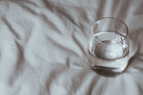 Free Minimalistic shot of a glass of water resting on a white duvet, taken indoors. Stock Photo
