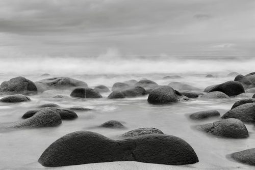 Free Tranquil black and white coastal scene with smooth stones and misty waves. Stock Photo