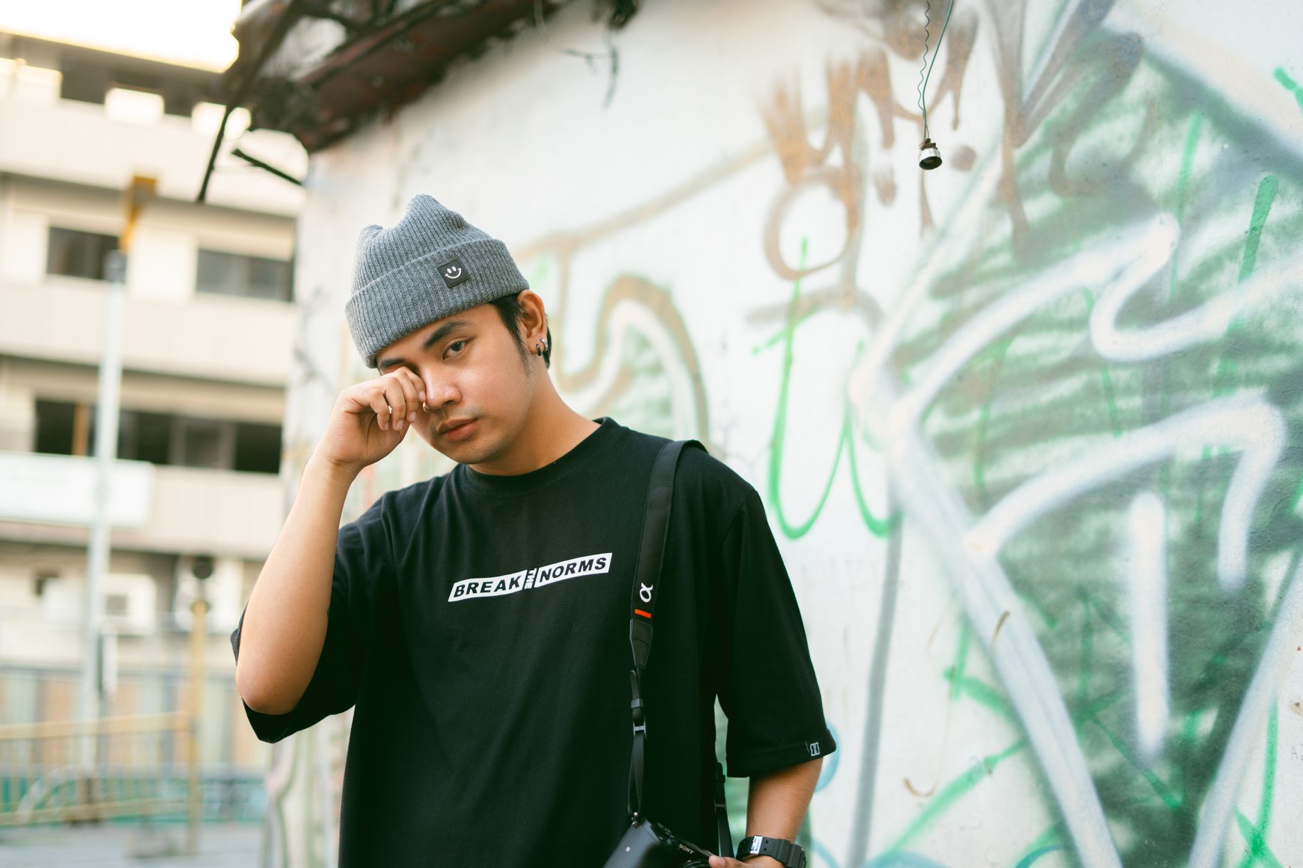Young man posing confidently in streetwear by a graffiti-covered wall in Maynila.
