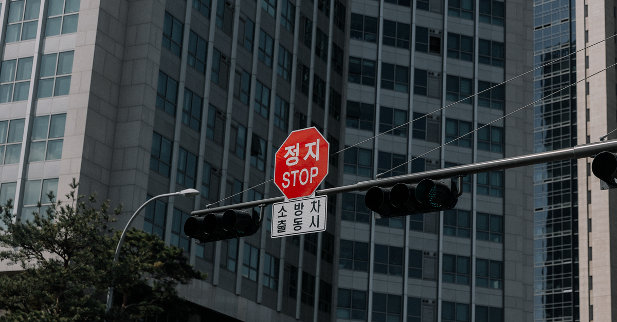 Stop sign with Korean script amidst tall modern buildings representing urban architecture.