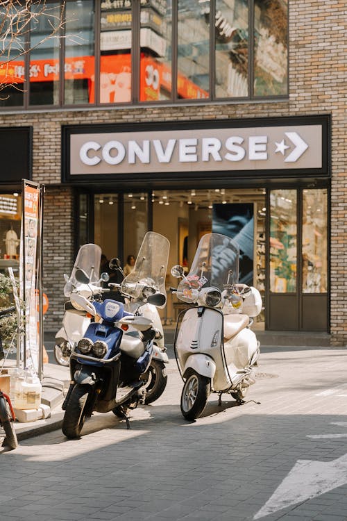 Two scooters parked in front of a converse store