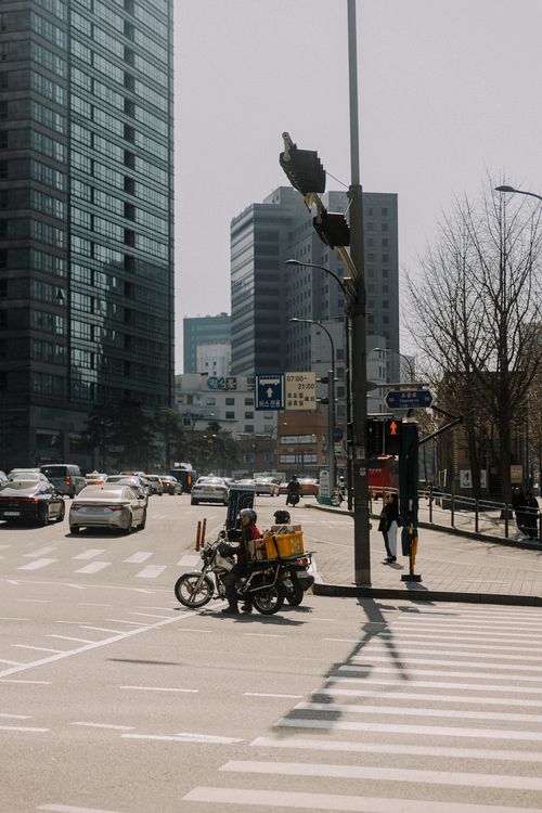Free Urban city intersection with motorbike and skyscrapers, showcasing bustling traffic during the day. Stock Photo