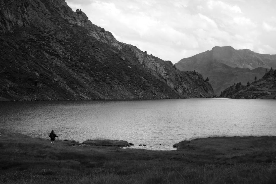 A tranquil mountain lake surrounded by rugged landscapes under a cloudy sky.