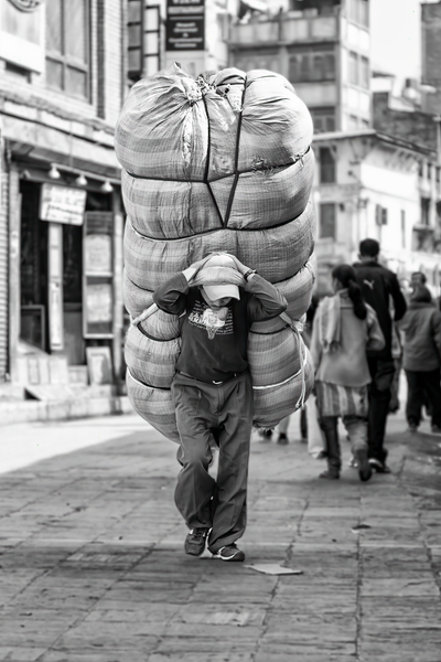 A man carrying a large bundle on his back down a busy street