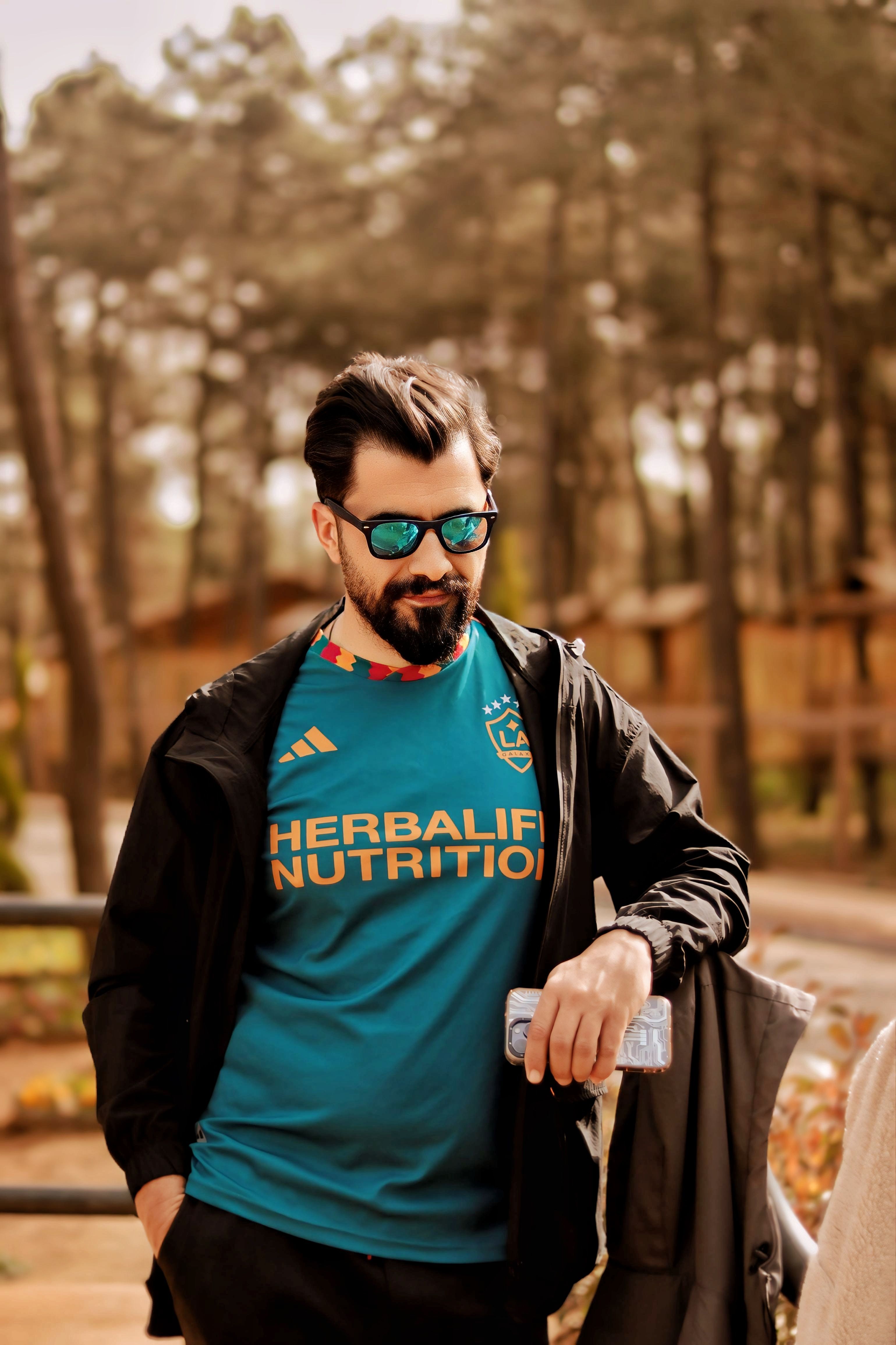 Casual man with sunglasses enjoying autumn park scenery while using smartphone.