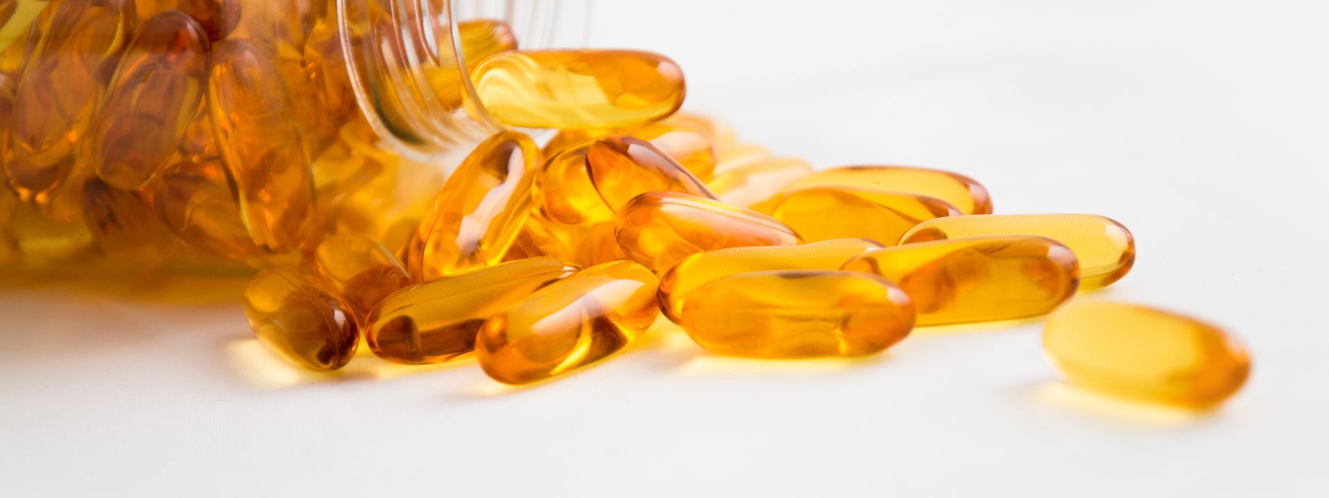 Golden fish oil capsules spilling from a clear bottle on a white background