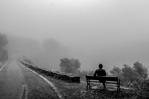 Free Black and white photo of a man sitting on a bench on a foggy road in Aydın, Türkiye. Stock Photo