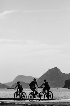 Three cyclists ride along a coastal path with scenic mountain views.