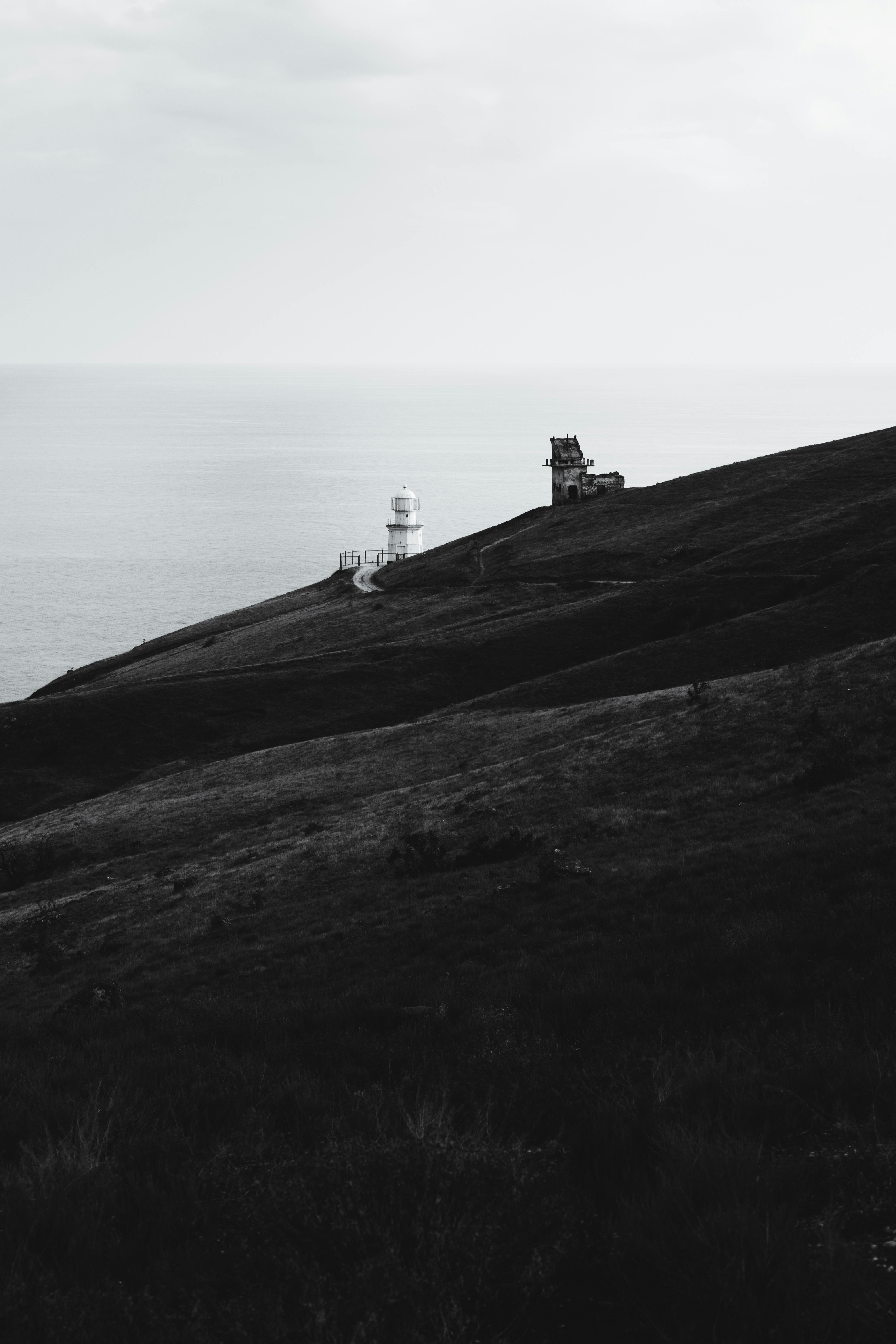 Dramatic black and white landscape featuring a lighthouse on a coastal hill under a cloudy sky.