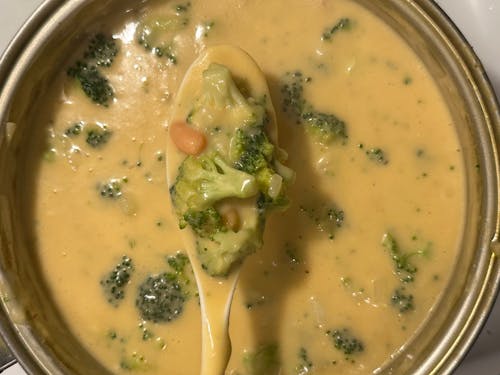 A spoon is holding a bowl of soup with broccoli