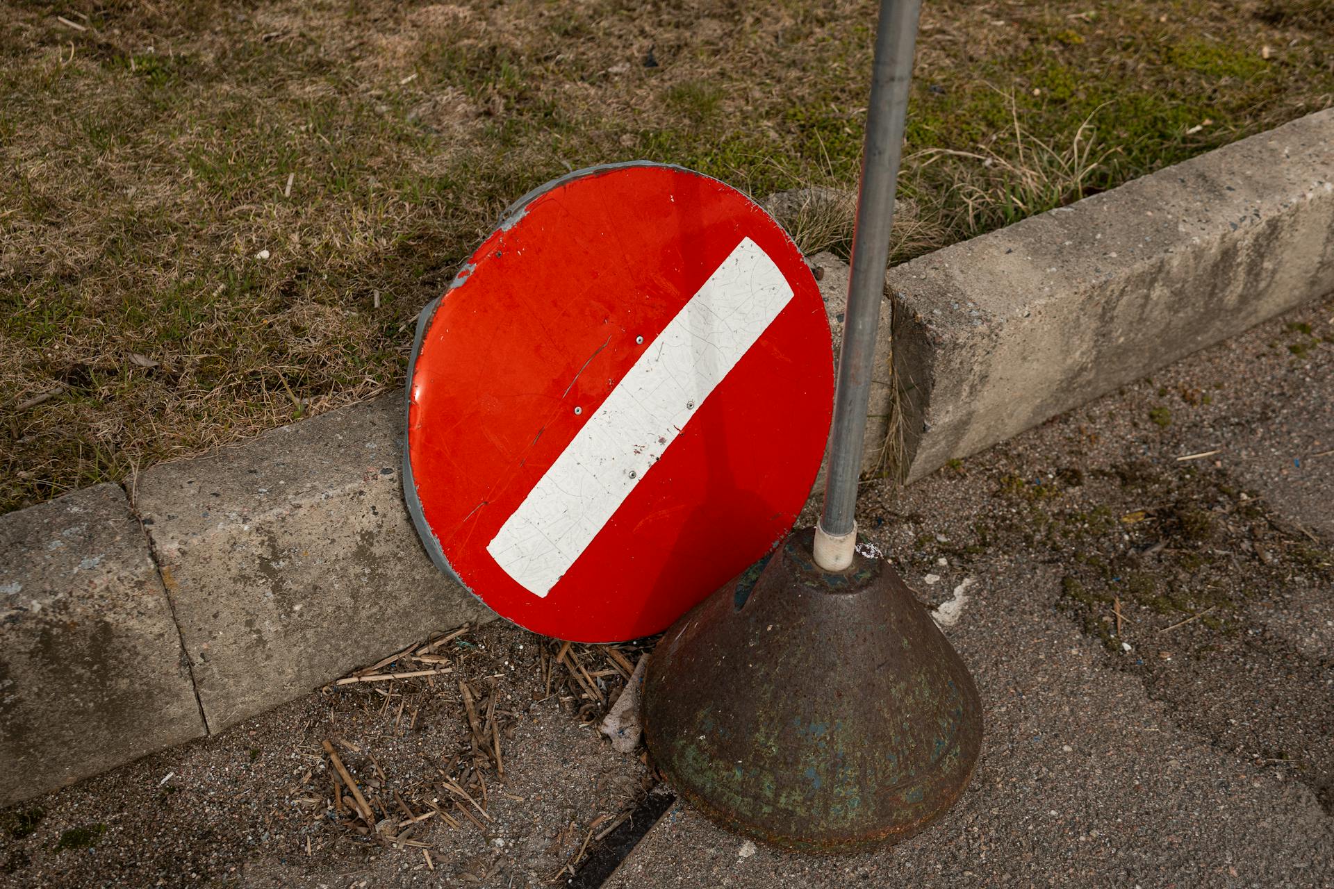 A broken red no entry sign leaning against a curb on a Tallinn street.