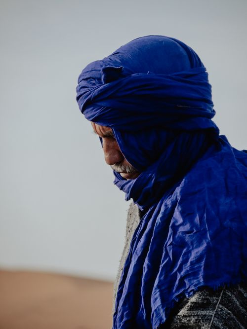 Free A thoughtful portrait of a man wearing a blue turban amidst the Moroccan desert sands. Stock Photo