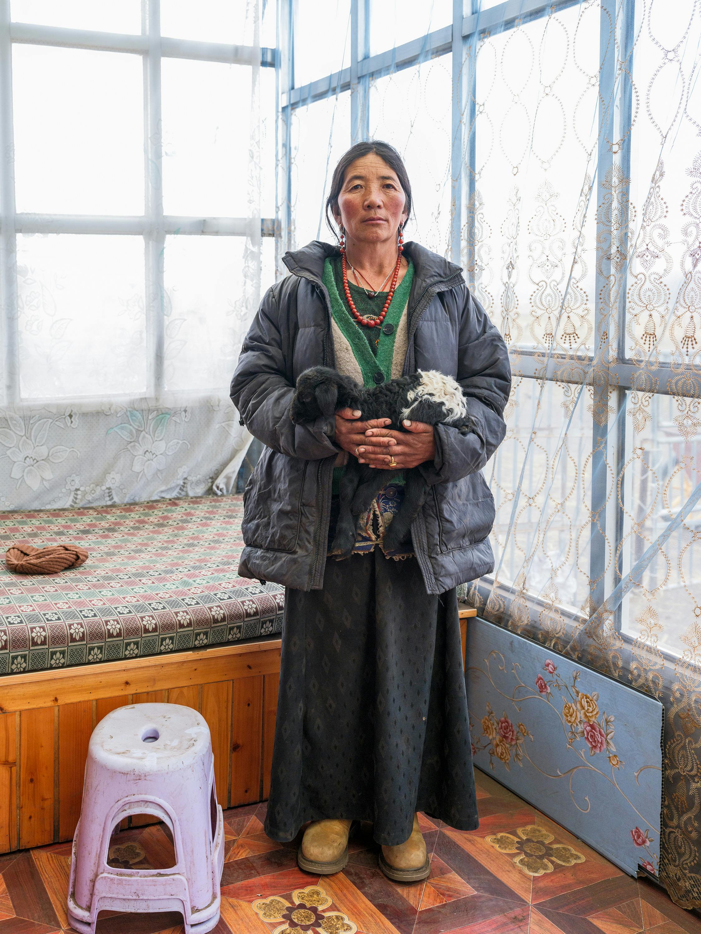 Mongolian woman in traditional attire holding a baby goat inside a cozy room.