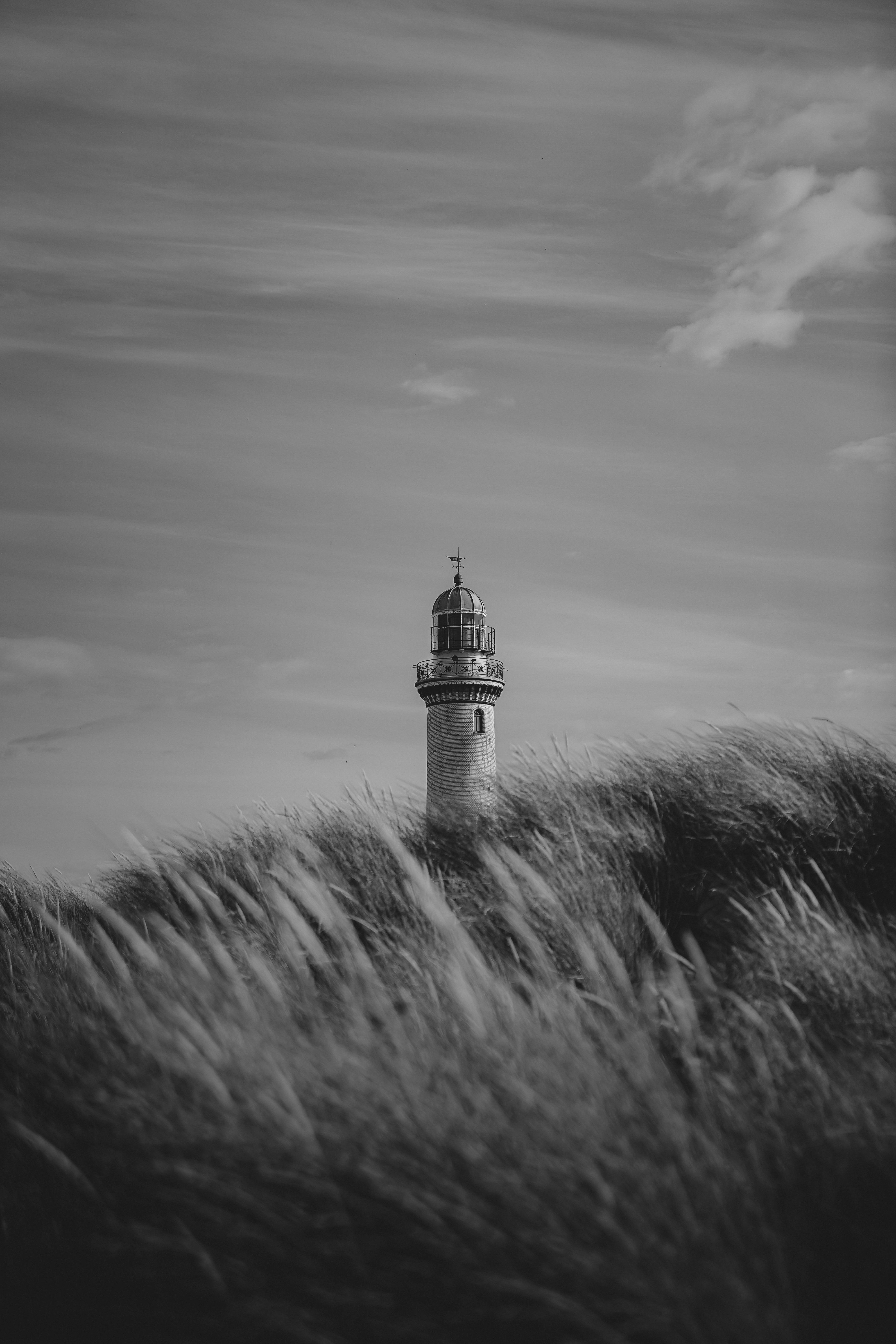 A peaceful black and white scene featuring a lighthouse amidst waving grass in Rostock.