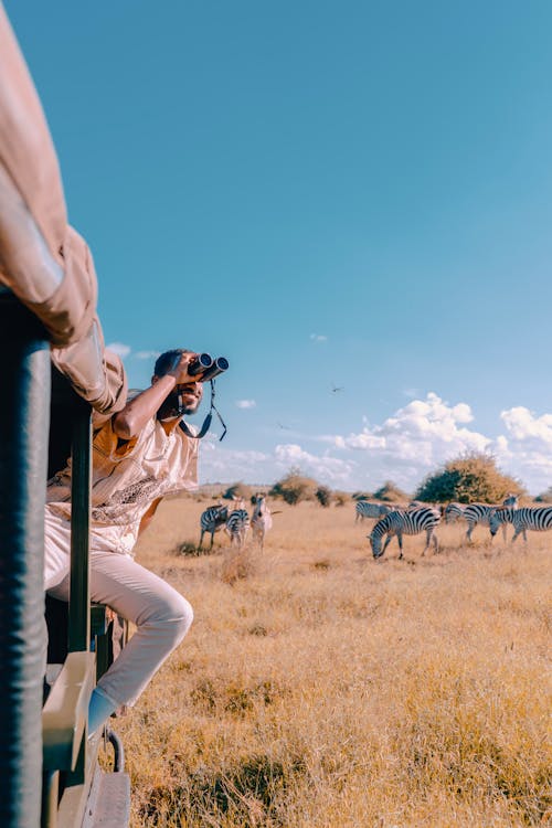 A woman is looking through binoculars at zebras