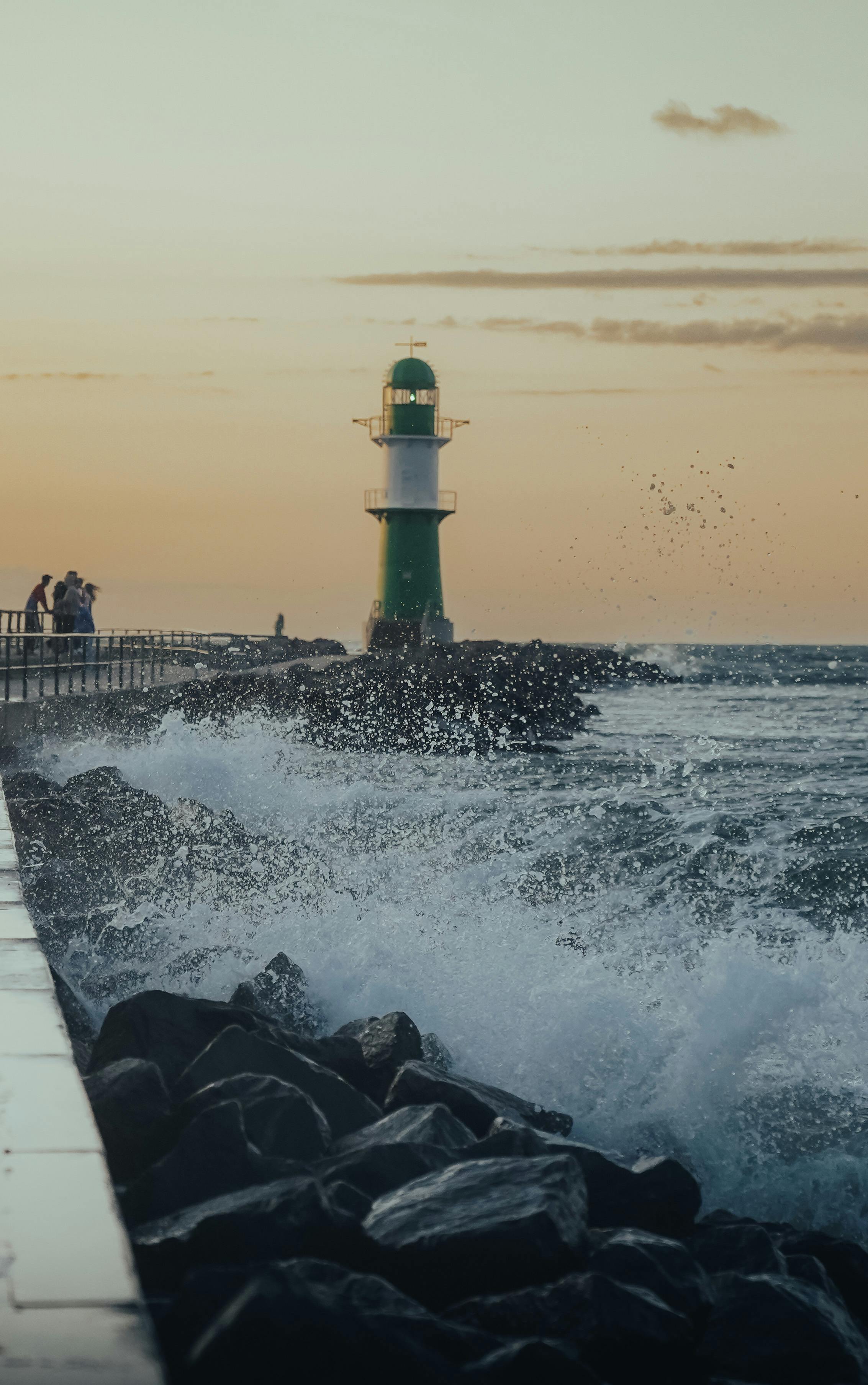 Scenic view of a lighthouse with crashing waves at sunset on the Baltic Sea in Rostock, Germany.