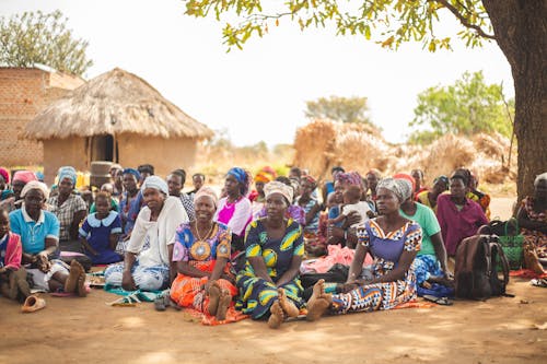 A group of women sitting on the ground in front of a hut