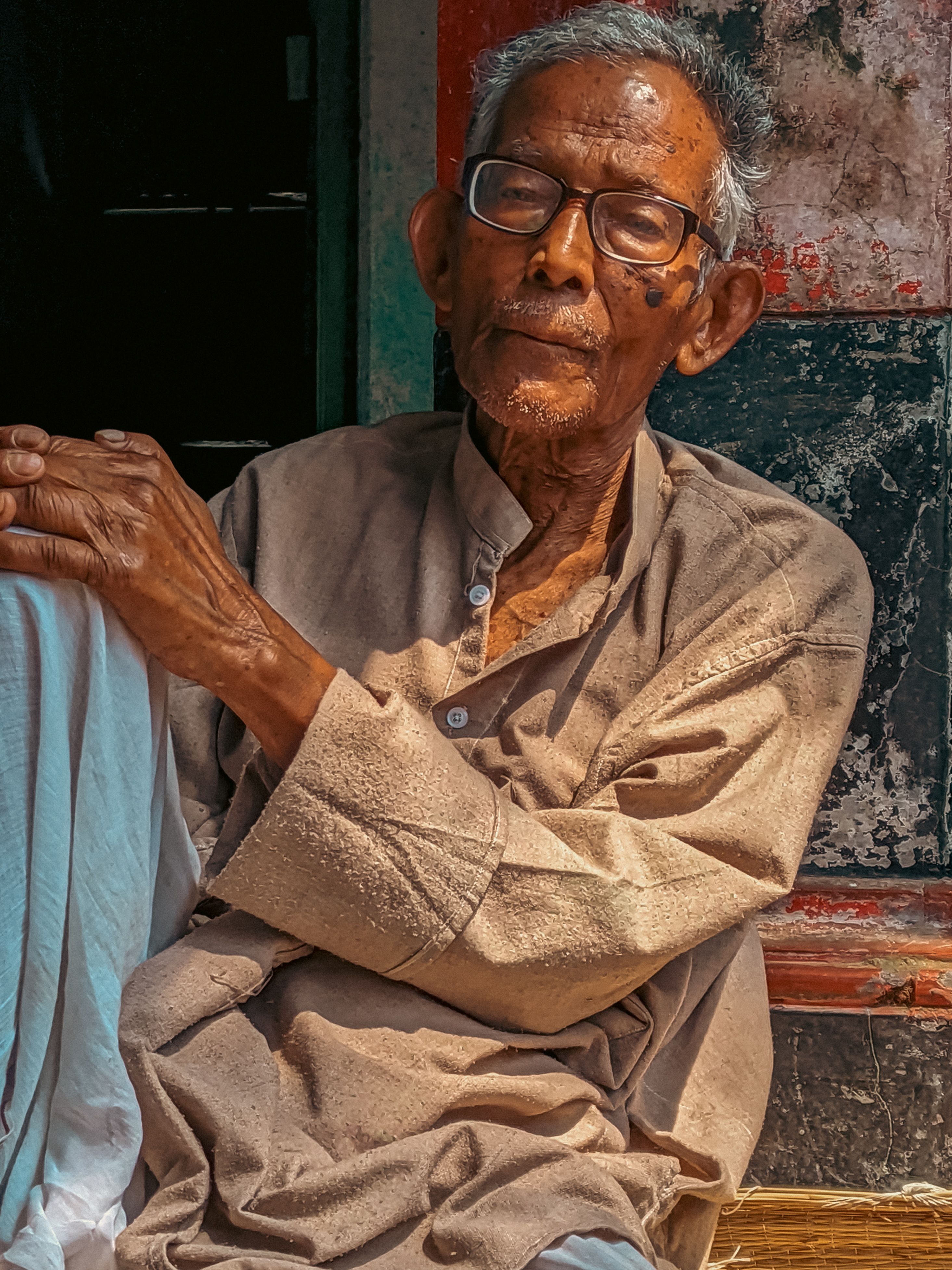Elderly man with eyeglasses sitting peacefully in Kolkata, India, enjoying the daylight.
