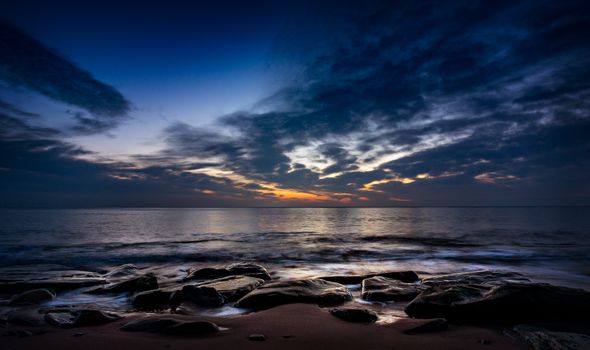 Captivating seascape of a sunset with dramatic skies, waves, and rocky shore.