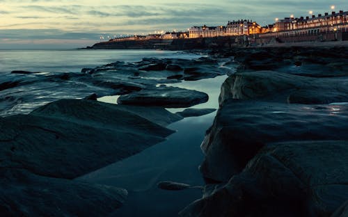 A view of the shoreline at dusk with buildings on the rocks