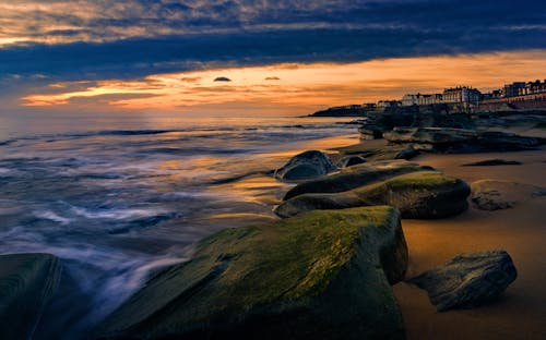 A sunset over the ocean with rocks and water