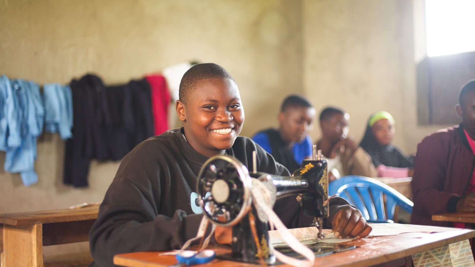 Happy student in Uganda using a sewing machine in class