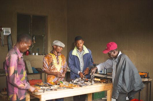 Group of men collaborating in a Ugandan workshop surrounded by tools and equipment.