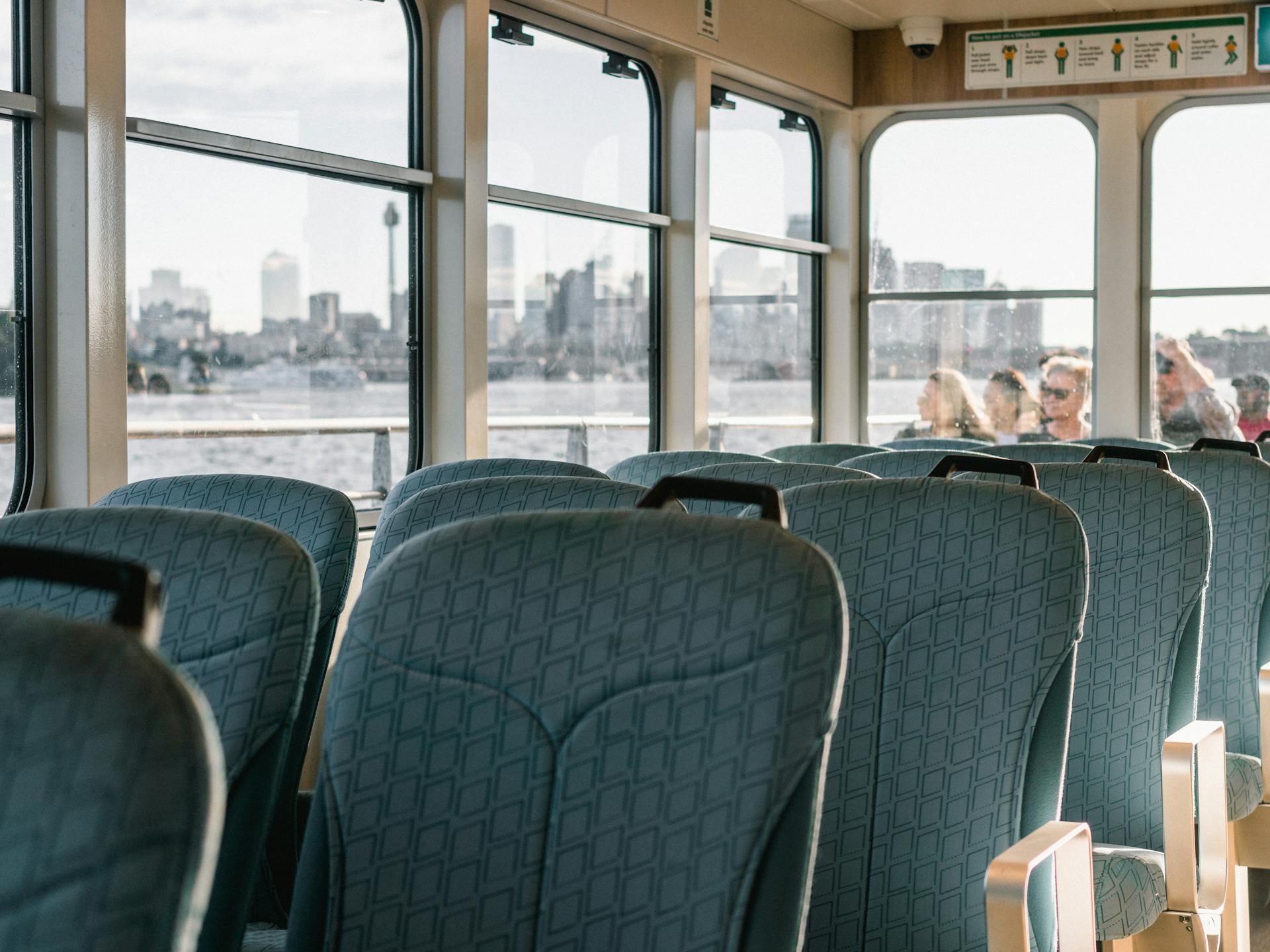 Interior of a passenger ferry with empty seats overlooking a city skyline across the water.